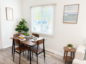 Ein Essbereich mit Tisch für vier Personen, einer Topfpflanze und einem Fenster mit Jalousien.