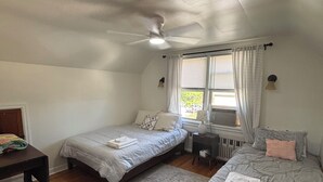 Un dormitorio con dos camas, un escritorio, una silla, un radiador y un ventilador de techo.