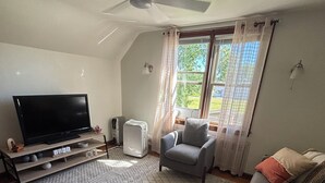 Una sala de estar con un televisor de pantalla plana, un ventilador de techo, un sofá gris y una alfombra estampada.