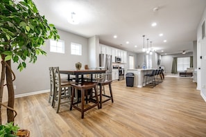 A spacious kitchen with modern appliances, a dining area with wooden chairs, and a bar area with stools. - Cozy 3BR Retreat Fast W-fi + Free Parking (Indianapolis)