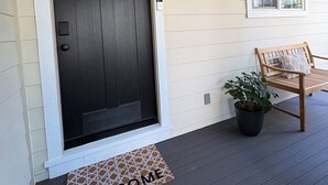 A house entrance with a dark door, a welcome mat, a bench, and a potted plant.