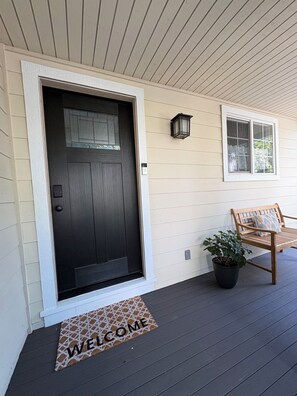 A house entrance with a dark door, a welcome mat, a bench, and a potted plant.