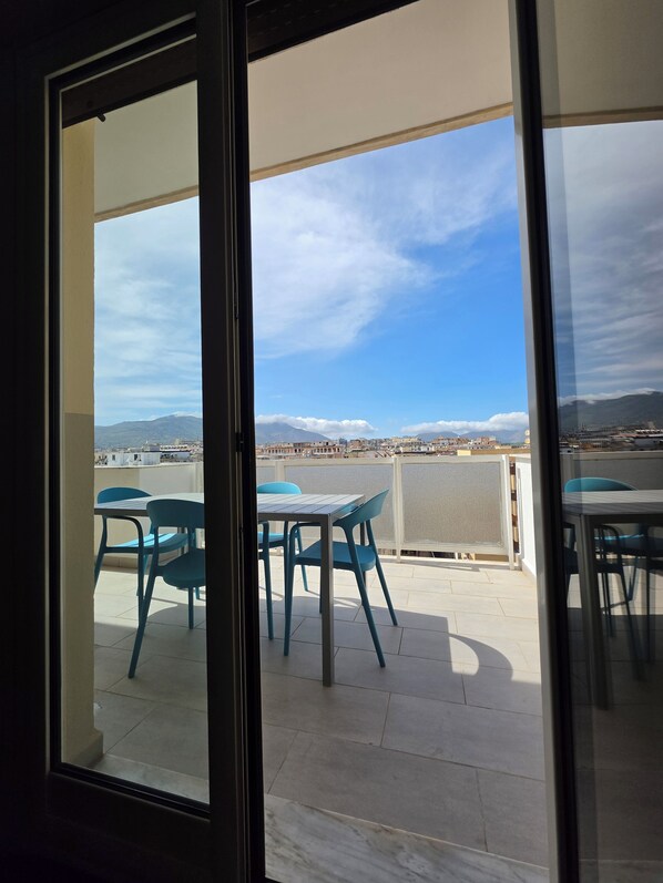 Ein Balkon mit Tisch und Stühlen, Blick aufs Meer und entfernte Berge.