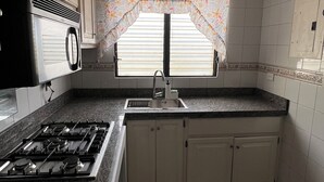 A kitchen with a gas stove, sink, and window with curtains. - Apartment (Santo Domingo)