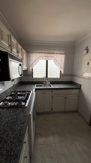 A kitchen with a gas stove, sink, and window with curtains. - Apartment (Santo Domingo)