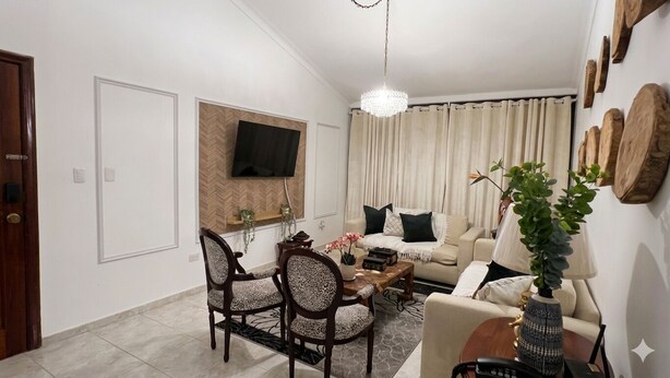 A living room with a sofa, chairs, a coffee table, a TV mounted on the wall, and a chandelier. - Apartment (Santo Domingo)