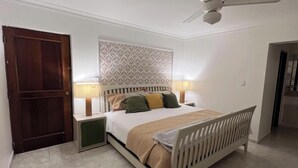 A bedroom with a bed, nightstands, a ceiling fan, and a door. - Apartment (Santo Domingo)