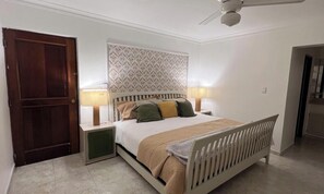 A bedroom with a bed, nightstands, a ceiling fan, and a door. - Apartment (Santo Domingo)