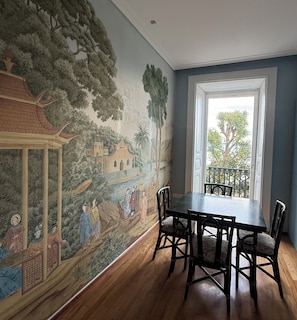 A dining area with a mural, wooden table, chairs, and a window with a view. - Luxury beachfront apartment (Napoli)
