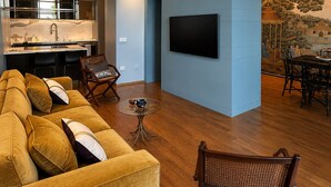 Een moderne woonkamer met een bank, stoelen, een eettafel, een keukenhoek en een aan de muur bevestigde televisie.