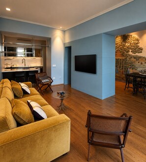 A modern living room with a sofa, chairs, a dining table, a kitchen area, and a TV mounted on the wall. - Luxury beachfront apartment (Napoli)