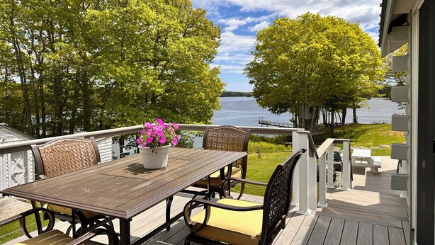 Um terraço com mesa e cadeiras, um vaso de planta e vista para um lago.