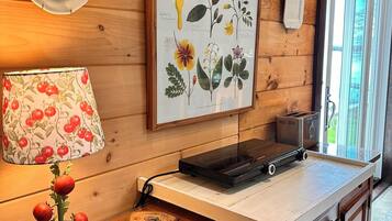 A wooden cabin interior with a kitchen counter, a framed botanical illustration, a lamp with cherry patterns, and a toaster.