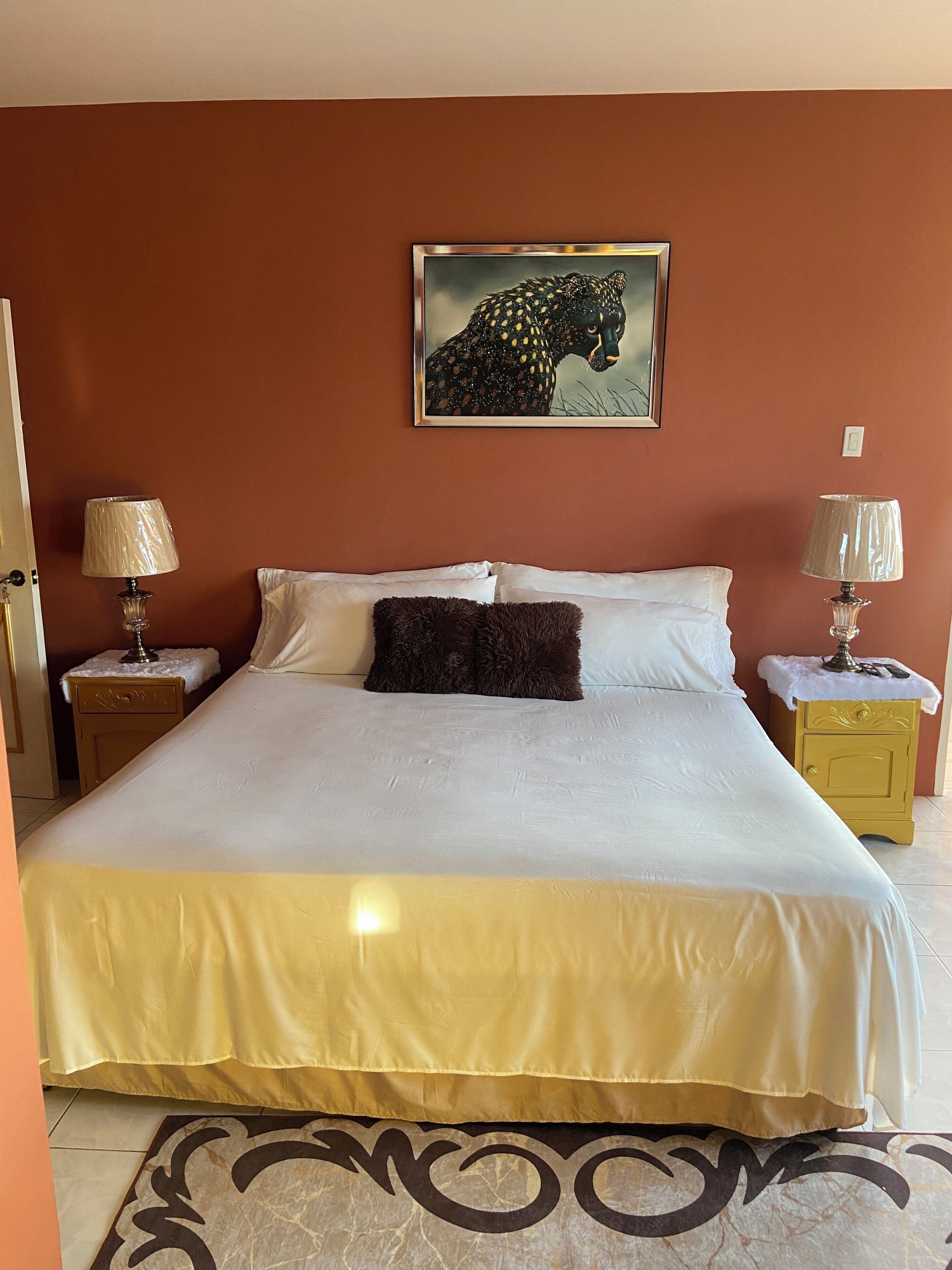 Ein Schlafzimmer mit einem großen Bett, zwei Nachttischen mit Lampen, einem Wandbild eines Leoparden und einem gemusterten Teppich.