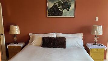 Ein Schlafzimmer mit einem großen Bett, zwei Nachttischen mit Lampen, einem Wandbild eines Leoparden und einem gemusterten Teppich.