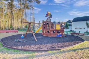 Ein Spielplatz mit einer Piratenburg-Spielanlage, umgeben von einer runden Mulchfläche, mit Bäumen und einem Gebäude im Hintergrund.