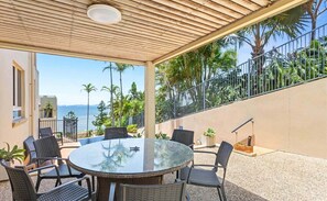 An outdoor patio with a round table and chairs, a wooden ceiling, and a view of palm trees and the ocean. - Four, Villa Mar Colina (Yeppoon)