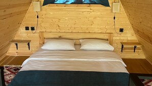 A wooden interior with a bed, a window with curtains, and two wall-mounted speakers. - Harmony Cottages Kazbegi  (Stepantsminda)