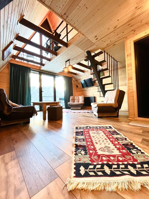 Amplia sala de estar estilo loft con techo alto, vigas de madera, un ventanal grande y una zona de estar acogedora.