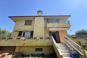 Un edificio de dos plantas con un balcón, una escalera y una ventana pequeña.