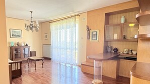 A spacious room with a wooden floor, a dining table, a chandelier, and a kitchen area with cabinets and a countertop. - C015 – Camerano – Three-story villa with garden (Camerano)