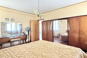 Un dormitorio con cama, cómoda, espejo, ventilador de techo y puerta corrediza que da a otra habitación.