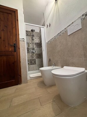 Une salle de bain avec une porte en bois, une douche avec une porte en verre et deux lavabos blancs.