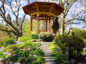 A gazebo with a red and yellow structure, surrounded by a garden with various plants and a stone staircase leading up to it. - 4 Star Holiday Home in Visby (Visby)