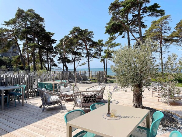 An outdoor seating area with tables and chairs, overlooking a beach and the sea. - 4 Star Holiday Home in Visby (Visby)