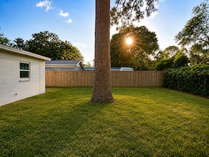 A residential backyard with a wooden fence, a tree, and a house. - 4BR Beach Getaway / 7 Min to Okaloosa Island / Fenced Yard / Sleeps 10 (Fort Walton Beach)