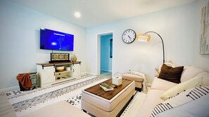 Ein Wohnzimmer mit Flachbildfernseher, einer Couch, einem Couchtisch und einer Wanduhr.