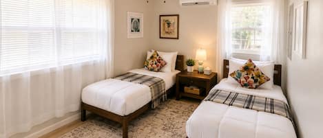 Un dormitorio con dos camas, ventilador de techo, aire acondicionado y una alfombra.
