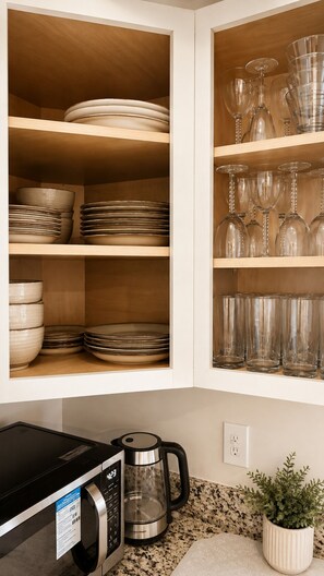 Une cuisine avec des étagères où sont rangées des assiettes et des verres, une machine à café et un four à micro-ondes.