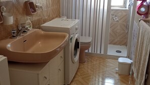 Ein Badezimmer mit Waschbecken, Toilette, Waschmaschine und Duschbereich.