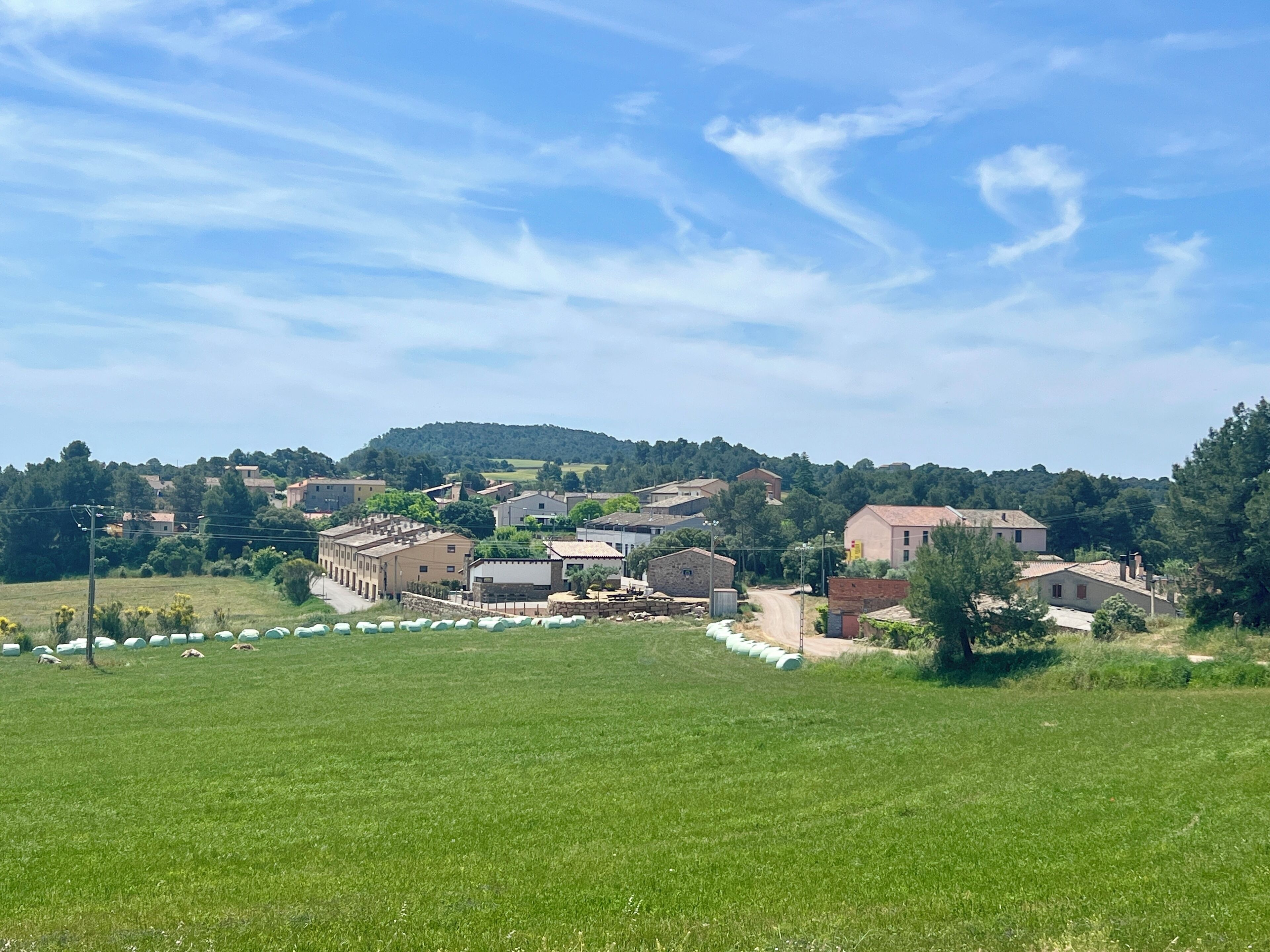 Un villaggio rurale con case, un campo verde e una collina sullo sfondo.