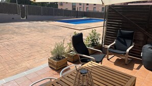 An outdoor patio with a pool, wooden furniture, and a pergola providing shade.