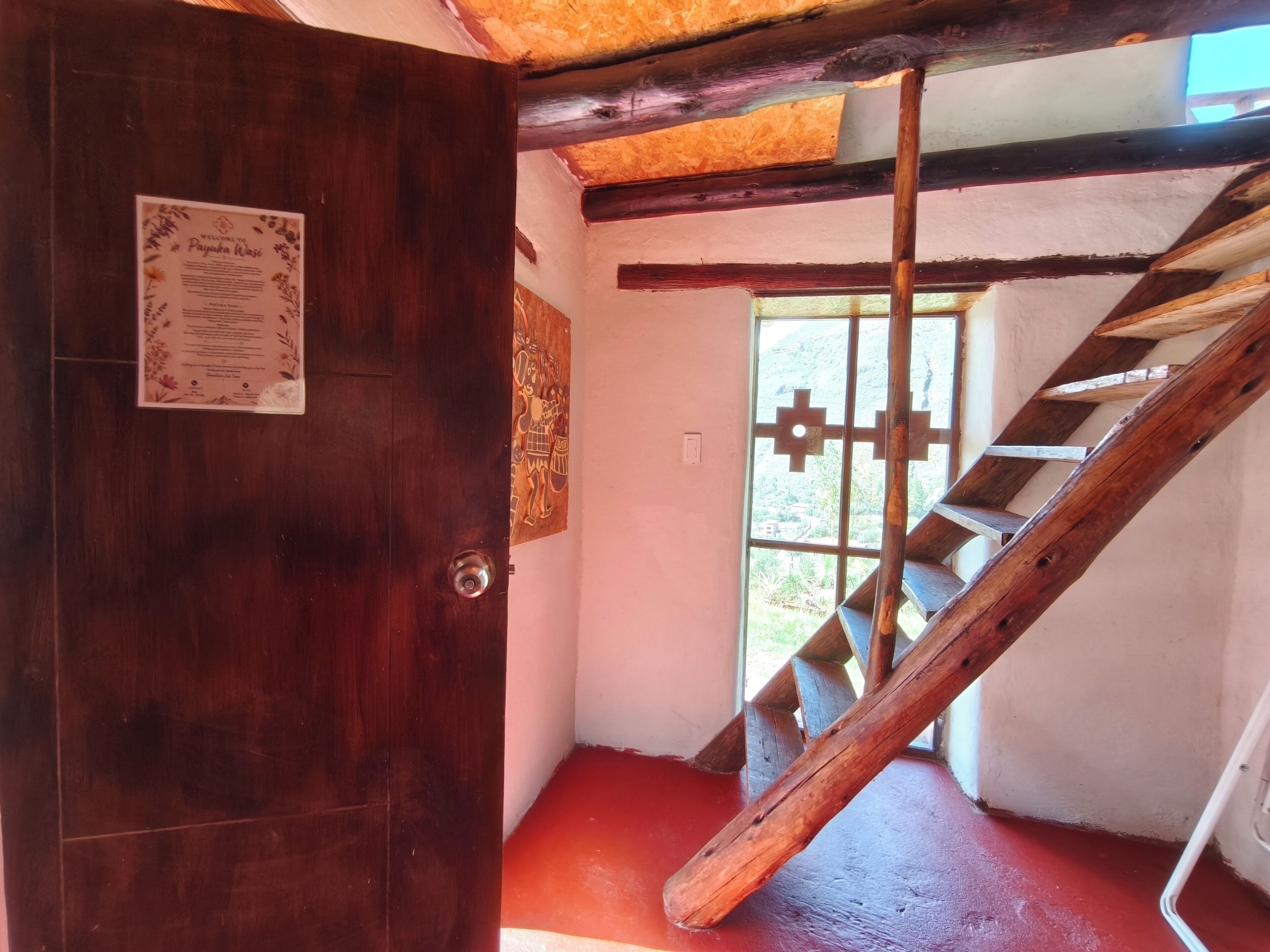 Una puerta de madera con un cartel, una escalera con barandilla de madera y una ventana con vistas a la vegetación.
