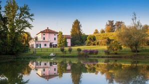 Ein großes, pinkfarbenes Gebäude mit Spiegelung in ruhigem Wasser, umgeben von Bäumen und einer grünen Wiese.