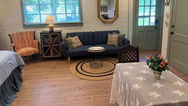 A cozy living room with a sofa, armchair, lamp, mirror, and a small table with a vase of flowers.