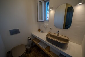 Un baño con lavamanos, espejo, ventana e inodoro.