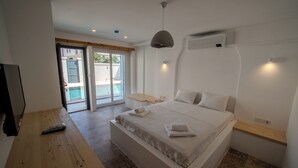 A bedroom with a large bed, a wooden nightstand, a remote control, and a sliding glass door leading to a balcony. - Mia Storia Alaçatı Hotel (Cesme)