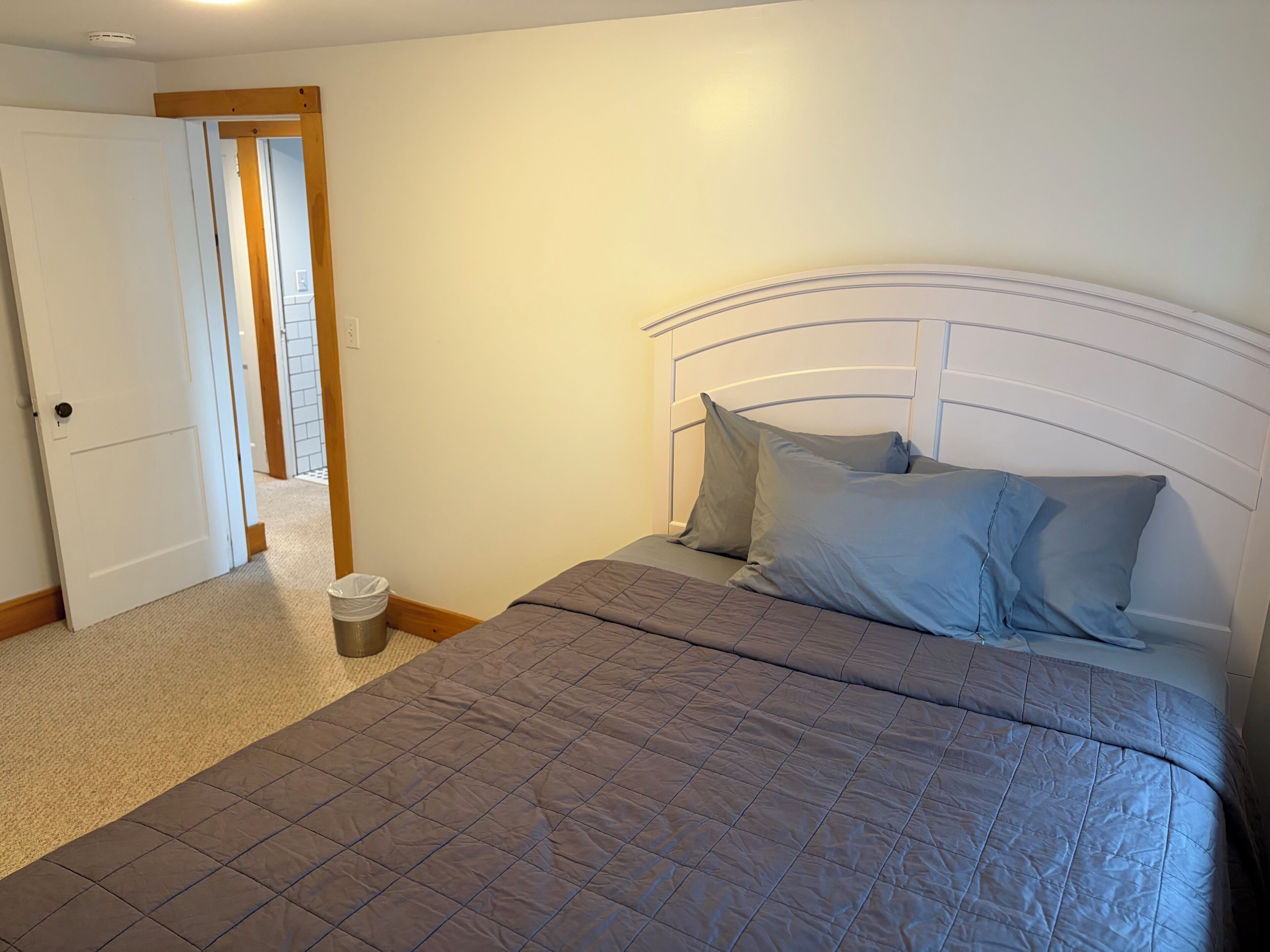 Une chambre à coucher avec un lit, une porte et une poubelle.