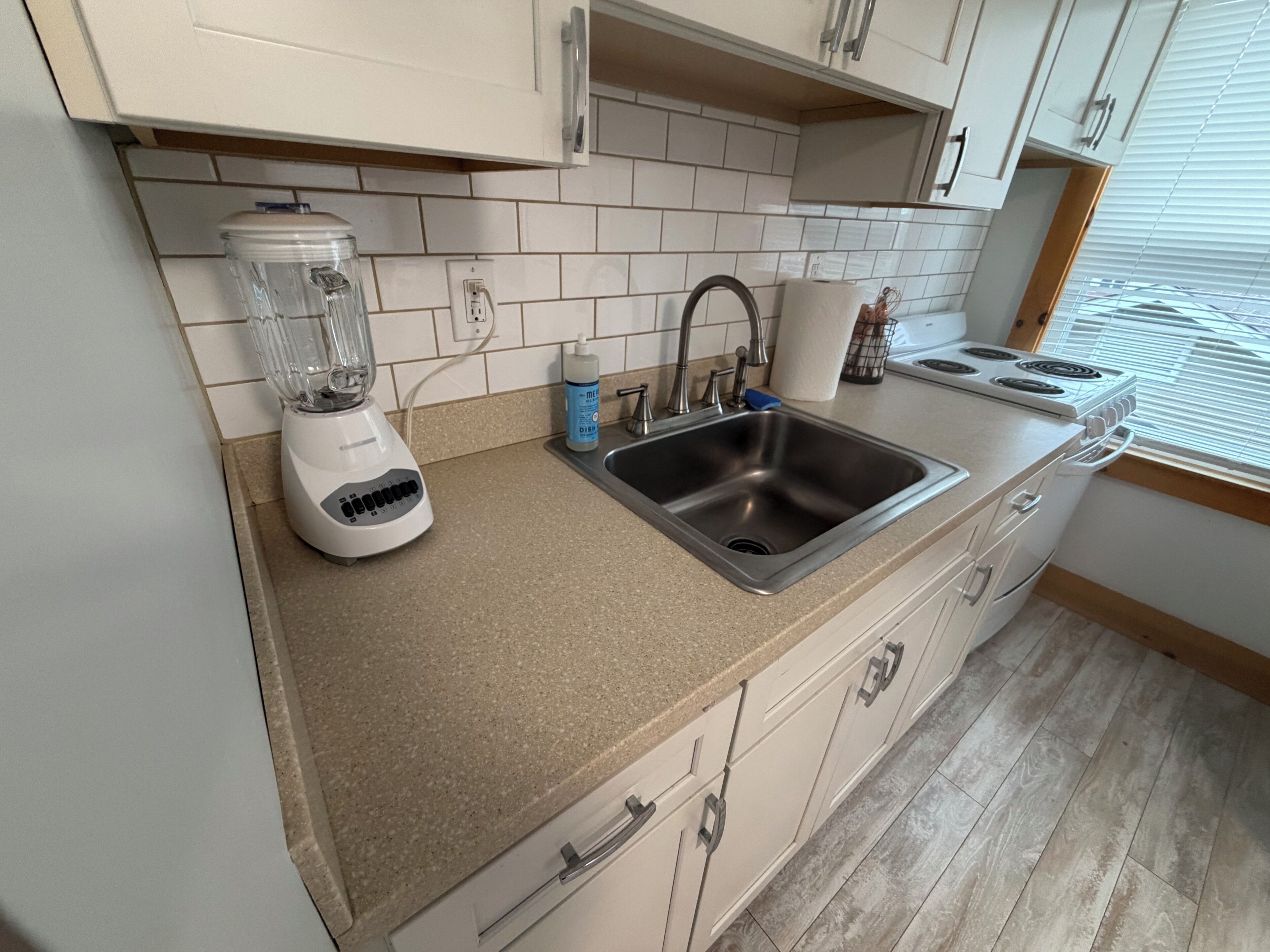 Una cocina con licuadora integrada, pileta de acero inoxidable y estufa.
