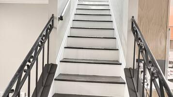 Un escalier avec des rampes noires et des marches blanches, menant à un palier où est accrochée une image encadrée.