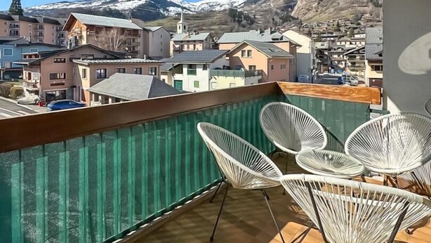 Un balcone con vista su una città e montagne, sedie bianche e una ventola.