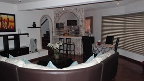 Ein Wohnzimmer mit einer Couch, einem Couchtisch mit einer Vase, einer Küchenzeile mit einer Arbeitsplatte und Stühlen, sowie einer Treppe, die in eine weitere Ebene führt.