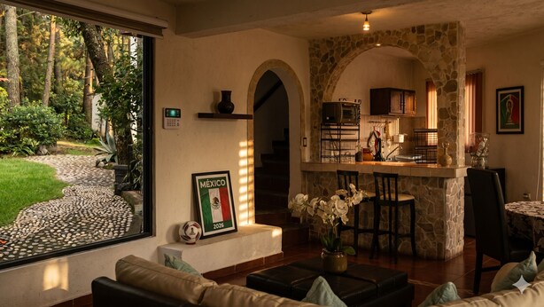 Ein gemütliches Wohnzimmer mit Kamin aus Stein, einem Essbereich mit Bar und Blick auf einen Garten durch große Fenster.