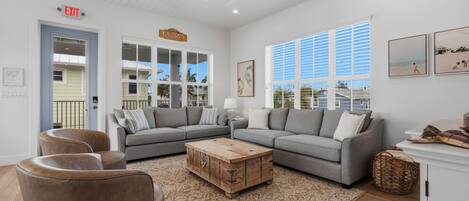A living room with a sectional sofa, a wooden coffee table, and a large window with blinds.