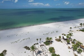 Ein Strand mit weißem Sand, Palmen und einem kleinen Gebäude.