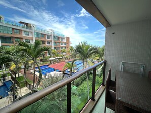 Ein Balkon mit Blick auf einen Swimmingpool, Palmen und ein mehrgeschossiges Gebäude.